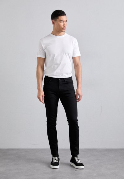 Černé skinny džíny v kombinaci s bílým bavlněným tričkem a černými teniskami, s jednoduchým designem a neutrální barevnou paletou.