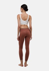 Soutien-gorge de sport côtelé gris clair associé à des leggings ajustés couleur rouille avec une taille lisse et une texture subtile.