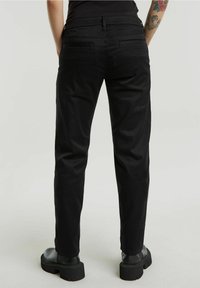 Pantalons noirs fuselés en mélange de coton lisse, avec une taille mi-haute et deux poches arrière, associés à des chaussures noires épaisses.