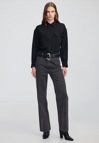 Czarna prążkowana koszula z srebrnymi zdobieniami, z dwoma kieszeniami na piersi, w połączeniu z ciemnoszarymi jeansami o wysokim stanie i czarnymi, spiczastymi botkami.