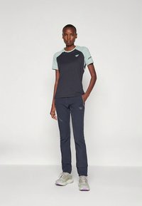 Marineblå og lys teal treningsantrekk med kortermet topp og tettsittende bukser. Toppen har kontrasterende skulderfarger og logoer.