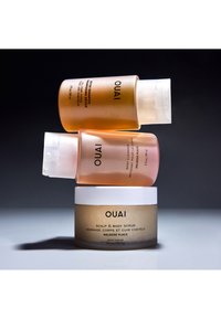 Trzy produkty do pielęgnacji skóry OUAI ułożone jeden na drugim: przezroczysta złota butelka z pompką, różowa butelka z pompką oraz słoiczek kremu z białą pokrywką i gładką konsystencją.
