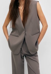 Grå ärmlös blazer i glatt tyg, med en djup V-urringning och två framfickor, kombinerad med matchande byxor.