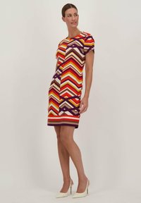 Multicolore zigzagpatroon jurk met korte mouwen, met warme tinten van rood, oranje en paars. Gemaakt van rekbaar materiaal, tot de knie.