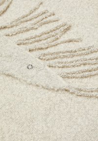 Tissu texturé beige clair avec des bords fringés et un détail métallique, présentant une apparence douce et moelleuse dans l'ensemble.