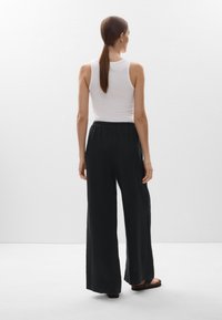 Fekete, bő szárú nadrág, húzózsinóros derékkal, könnyű anyagból, egy testhezálló fehér ujjatlan toppal párosítva.