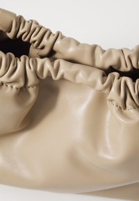 Bežová taška z umělé kůže se staženými okraji, s hladkým povrchem a lehkým designem. Minimalistická estetika bez viditelné kovové výbavy.