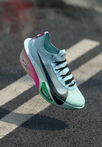 Light blue athletic shoe with a textured knit upper, black accents, green and pink details on the sole, and a streamlined silhouette.