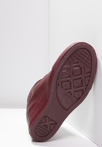 Scarpa bordeaux con suola in gomma texturizzata, caratterizzata da un motivo a diamante e logo in rilievo. Il materiale superiore appare liscio con cuciture sovrapposte.