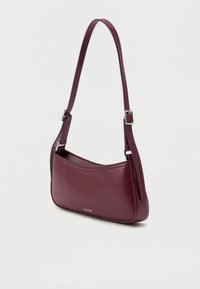 Burgundowa skórzana torba na ramię o gładkiej fakturze, z jedną regulowaną rączką i subtelnym detalem logo z przodu.