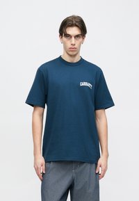 Μπλε ναυτικό βαμβακερό t-shirt με στρογγυλή λαιμόκοψη και κοντά μανίκια· διαθέτει λευκό κείμενο "CARHARTT" στο αριστερό στήθος· ομαλή υφή.