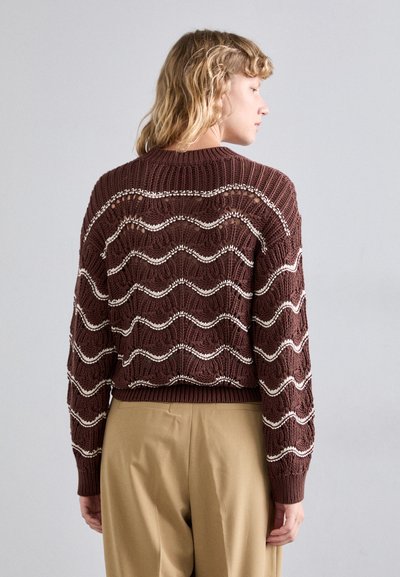Brun strikket sweater med bølgemønster og hvide accenter. Korte ærmer med ribbede manchetter og kant, med åben strikketekstur.