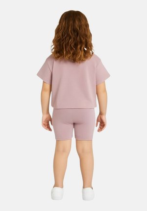 Ensemble deux-pièces en coton violet clair comprenant un haut court à manches courtes et un short vélo assorti. Des chaussures blanches à enfiler complètent le look.