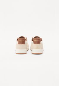 Beige Wildledersneaker mit braunen Lederakzenten an der Ferse, weißer Zwischensohle und Gummilaufsohle. Goldenes "REPLAY"-Logo auf der Rückseite.