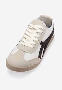 Beige und weiße Sneaker mit einer strukturierten Oberseite, ausgestattet mit cremefarbenen Schnürsenkeln, braunen Akzenten und einer Gummisohle. Klassisches sportliches Design.