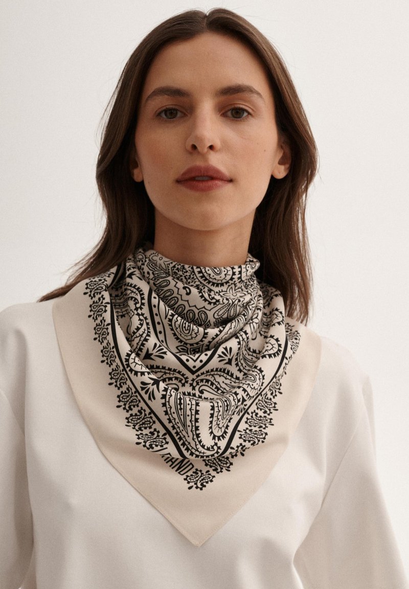 Kwadratowy szalik z czarnym wzorem paisley na beżowym tle, o gładkiej teksturze materiału i wykończonych brzegach.