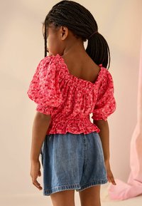 Rød blomstret bluse med puffede ærmer, samlet halsudskæring og elastisk talje, parret med højtsiddende denimshorts med frynset kant.