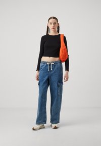 Top negro de manga larga recortado, pantalones cargo de mezclilla azul holgados con cintura ajustable, zapatos slip-on blancos y un bolso de hombro acolchado naranja.
