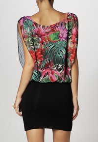 Luźna, wielokolorowa bluzka w kwiaty wykonana z lekkiego materiału, zestawiona z dopasowaną czarną mini spódnicą. Posiada okrągły dekolt i zwiewne rękawy.