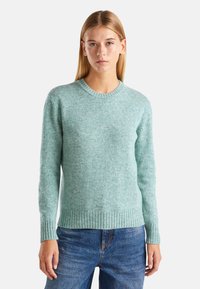 Jasnoniebieski sweter z dzianiny z okrągłym dekoltem, ściągaczami przy mankietach i dole. Miękka textura i lekko luźny krój, połączony z dżinsowymi spodniami.