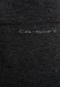 Black sock with a smooth, knitted texture. Features a subtle logo detail in light gray near the cuff. Ribbed design for fit and comfort.