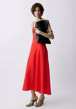 Rochie roșie fără mâneci, cu o siluetă fluidă, asortată cu o geantă de mână neagră, structurată, și mule cu toc cu model de șarpe. Eleganță simplă.
