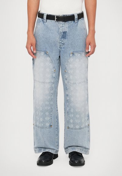 Pantalones de mezclilla anchos de color azul claro con bolsillos decorativos, un sutil patrón floral, acentos de latón y un cinturón negro en la cintura.