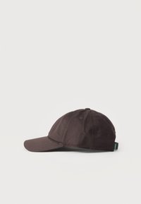 Casquette de baseball marron foncé à six panneaux, visière incurvée et une petite étiquette verte sur le bord arrière.
