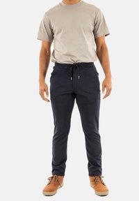 Camiseta de manga corta gris combinada con pantalones jogger azul marino que cuentan con una cinturilla elástica y cordón, usados con botas marrones con cordones.