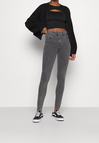 Grå högmidjade skinny jeans med en texturerad yta, kombinerat med en svart kort topp och en kraftig svart cardigan. Svarta sneakers fulländar looken.