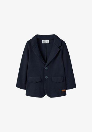 Tumši zils mazuļu izmēra žakets ar diviem priekšējiem pogām, ar iegrieztiem apkaklītes galiem, kabatām ar atloci un mazu brūnu zīmola etiķeti uz apmalēm.