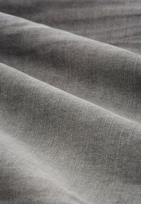 Tela gris con textura visible y pliegues suaves, capturando la luz y las sombras, creando una apariencia suave y acogedora.
