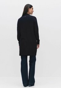 Zwarte lange mouwen cardigan met een rechte snit, textuurstof en een subtiele knoopdetail aan de achterkant, gecombineerd met blauwe flared jeans.