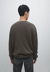Maglione a coste verde oliva scuro con colletto rotondo e maniche lunghe, caratterizzato da un motivo a maglia testurizzato e una vestibilità rilassata.