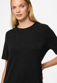 Camiseta negra de manga corta con una tela texturizada que presenta un sutil brillo, escote redondo y un ajuste relajado.