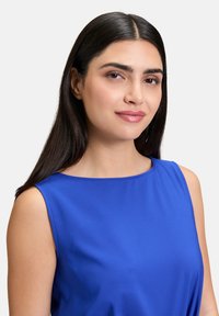 Modrá bezrukávová blúzka s okrúhlym výstrihom, vyrobená z hladkej tkaniny. Má jednoduchý dizajn bez viditeľných vzorov alebo akcentov.