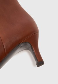 Chaussure à talons hauts en cuir marron avec un bout pointu et un élégant talon noir. Texture lisse avec des détails de couture subtils sur les côtés.