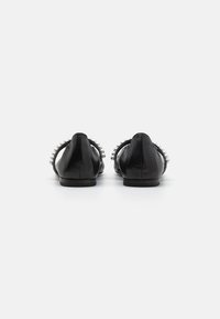 Chaussures en cuir noir avec un dos bas, ornées d'une sangle décorée de fausses perles le long du talon. Texture lisse et silhouette simple.