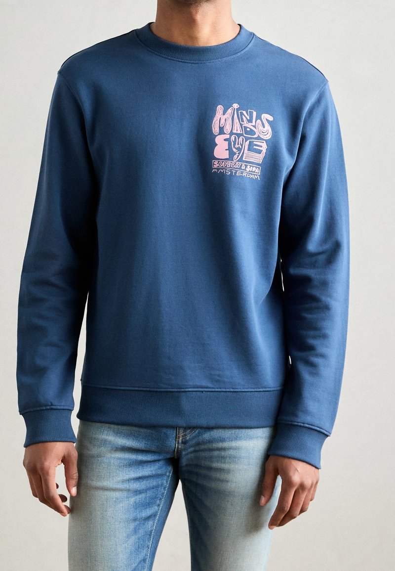 Niebieska bluza wykonana z miękkiego materiału, z różowym nadrukiem i napisem. Długie rękawy oraz ściągacze na mankietach i dole. Casualowy krój.