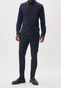 Mörkblå långärmad skjorta, knäppning fram, slim fit, i kombination med svarta byxor och svarta loafers. Släta tyger, klassisk design, rena linjer.