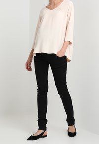 Blusa rosa chiaro, morbida e con scollatura a V e maniche a tre quarti; abbinata a jeans neri aderenti e scarpe flat nere.