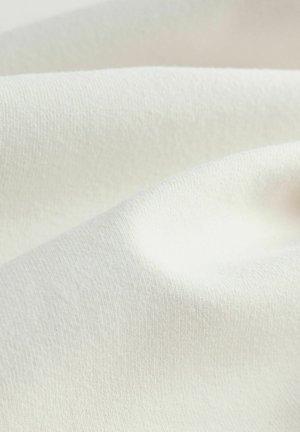 Crème-kleurige stof met een gladde, zachte textuur; heeft een subtiel geribd patroon en valt in zachte plooien.