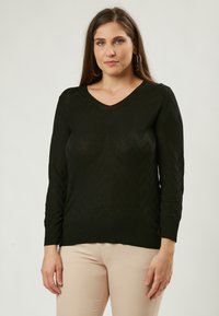 Schwarzer V-Ausschnitt-Pullover mit langen Ärmeln und Zick-Zack-Muster; aus leichtem Strickstoff; gerippte Bündchen und Saum. Kombiniert mit beigen Hosen.