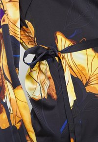 Blumenmusterstoff in Schwarz, mit gelben und braunen Farbtönen. Beinhaltet eine gebundene Schärpe in der Taille mit einer strukturierten Oberfläche.