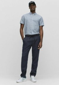 Korte mouwen, lichtblauw gestreept overhemd met knopen, gecombineerd met donkerblauwe, relaxte broek en witte sneakers met groene accenten.
