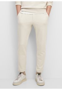Lichtbeige sweatpants met een relaxte pasvorm, voorzien van zijzakken en boorden bij de enkels. Gecombineerd met lichtgekleurde sneakers.