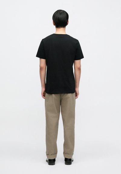 Μαύρο βαμβακερό t-shirt με στρογγυλή λαιμόκοψη, εμφανιζόμενο από πίσω. Φορεμένο με χακί παντελόνι και μαύρα παπούτσια, με γυρισμένα μανσέτα.