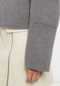 Γκρι μάλλινο πουλόβερ με κουτί σχεδίασης και φαρδιά μανίκια, συνδυασμένο με φούστα από κρεμ δέρμα με πλαϊνό φερμουάρ.