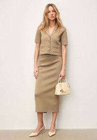 Robe en maille beige avec une taille cintrée, des manches courtes et un col en V. Associée à un petit sac à main beige et à des escarpins slingback pointus assortis.