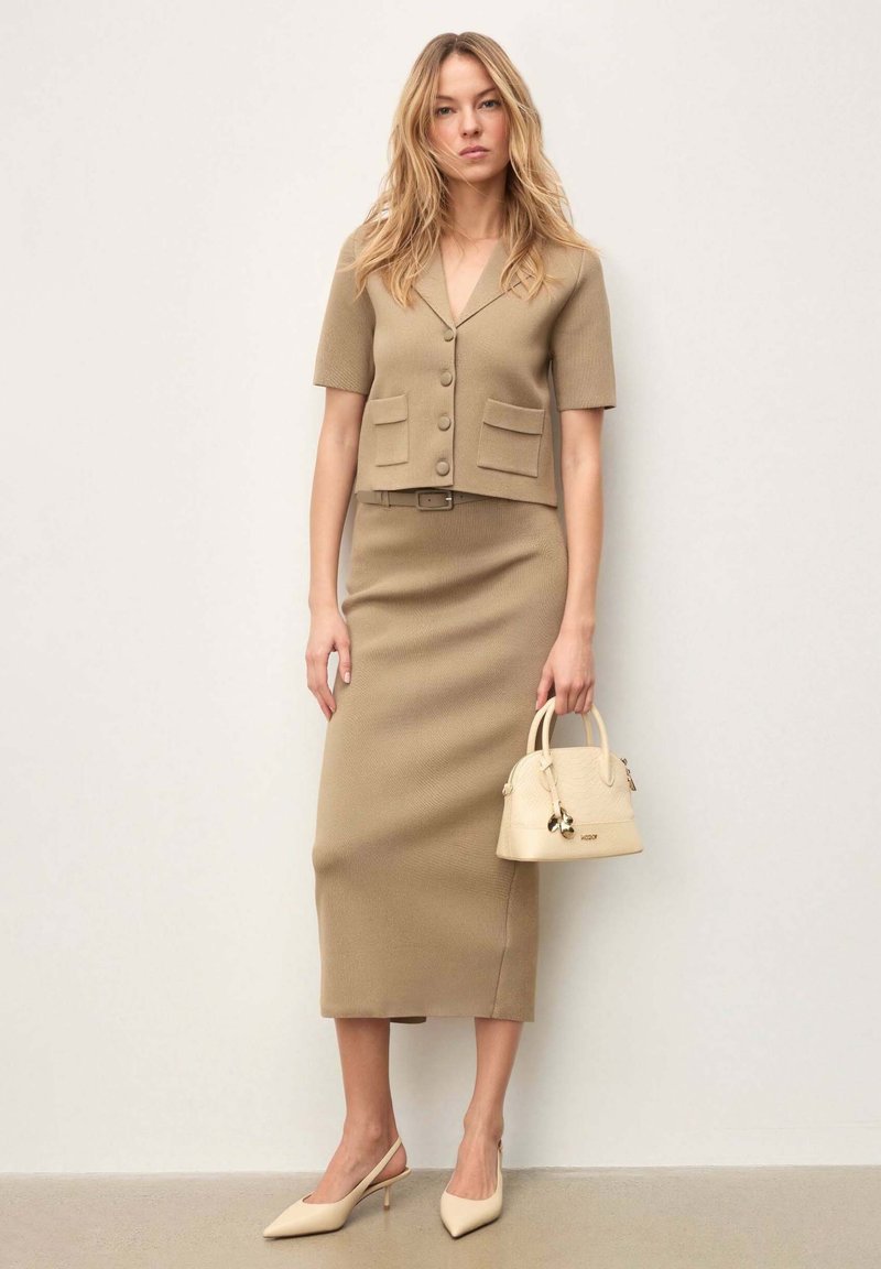 Robe en maille beige avec une taille cintrée, des manches courtes et un col en V. Associée à un petit sac à main beige et à des escarpins slingback pointus assortis.